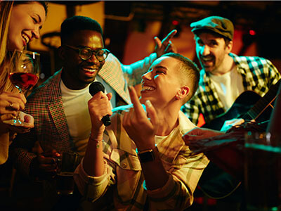 Group of happy friends enjoying while singing on microphone in a bar at night.