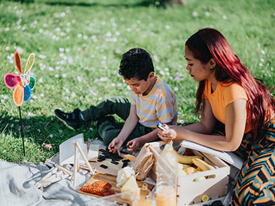 A Filipino mother and her child engage in fun activities during a family picnic outdoors. The scene showcases bonding, nature, and leisure moments in a green park under bright and sunny weather.